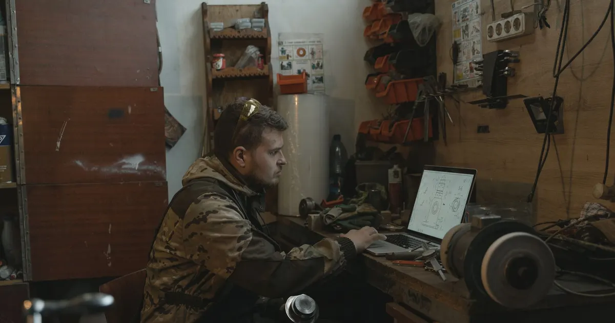 Artisan de profil devant son ordinateur portable posé sur un établi d atelier, pour étudier un abonnement référencement mensuel