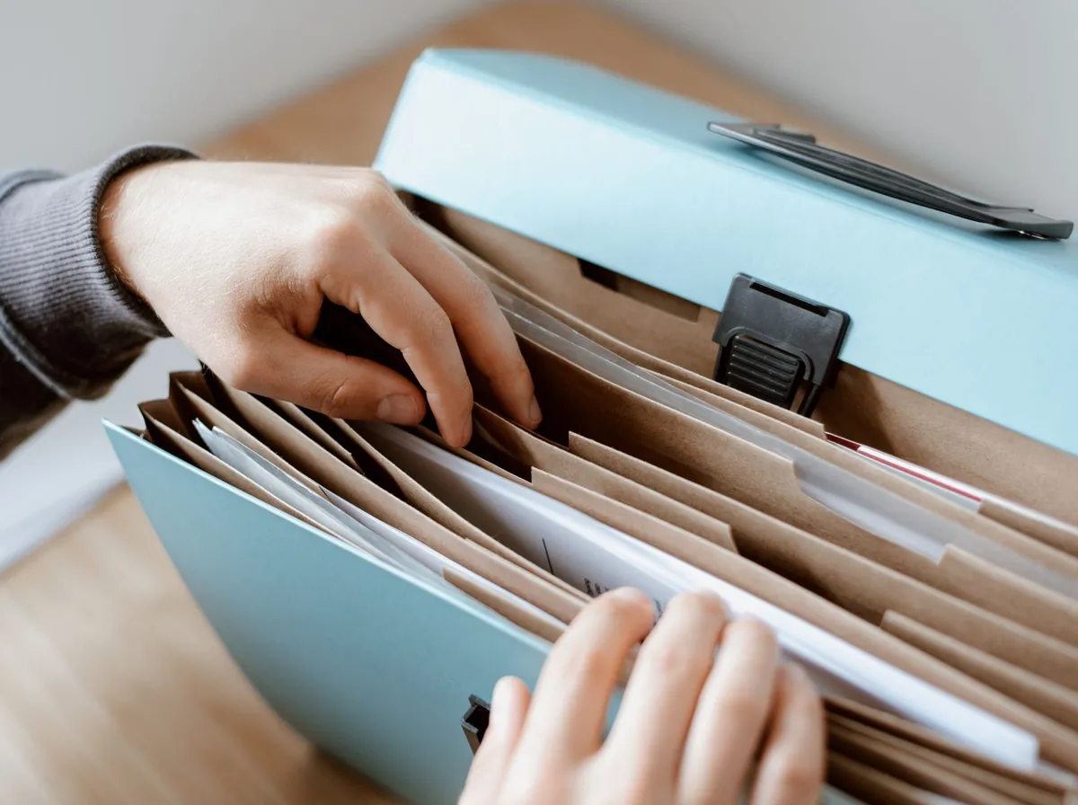 Main fouillant dans une boîte à dossiers suspendus pour retrouver un document administratif