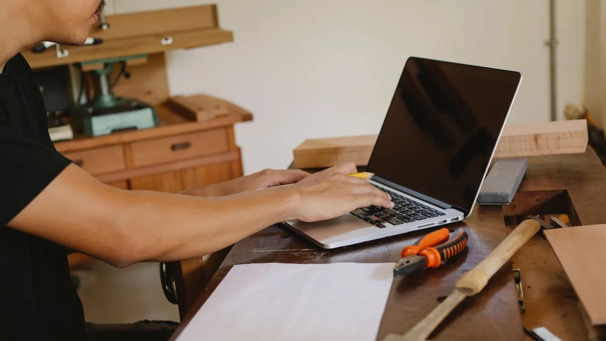 Artisan de profil consultant son ordinateur portable dans un atelier bois, outils sur l'établi, budget présence digitale complète artisan