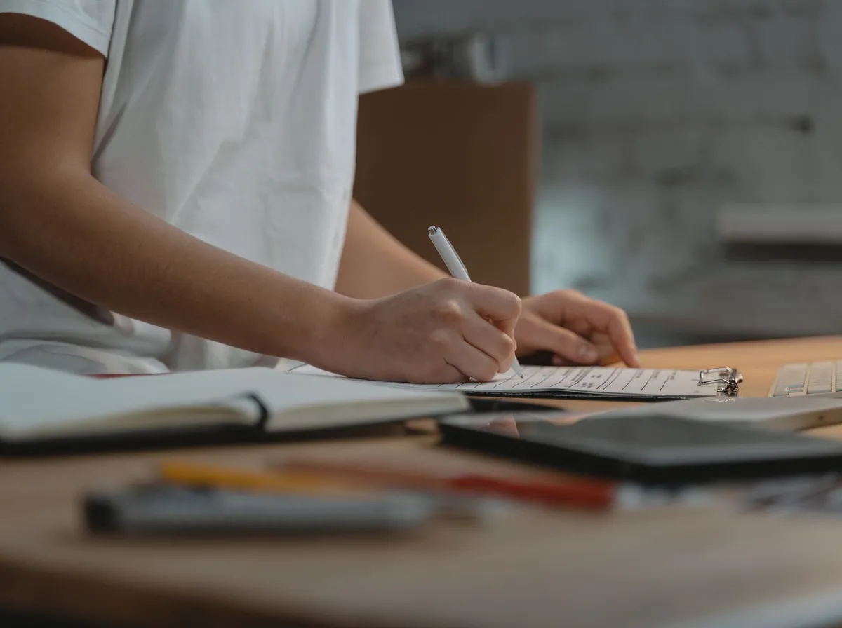 Main écrivant une liste de vérification sur un bureau en bois avant de choisir une agence web