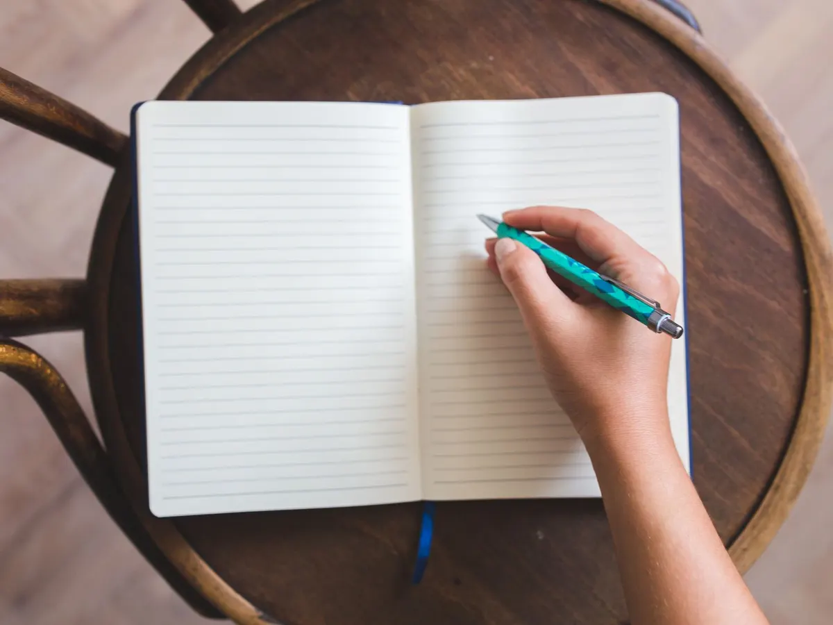 Main qui écrit dans un carnet ouvert posé sur un tabouret en bois, pour cocher la liste avant la refonte