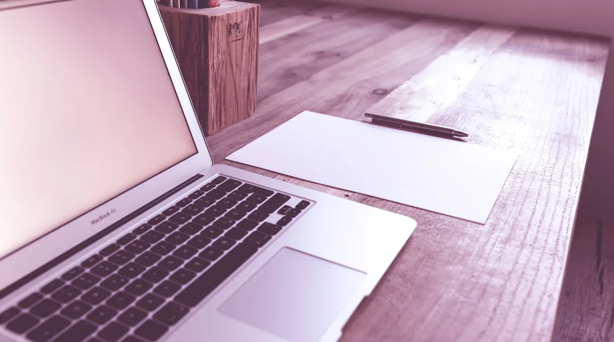 MacBook ouvert sur un bureau en bois clair, feuille blanche et stylo à côté, performance site internet artisan