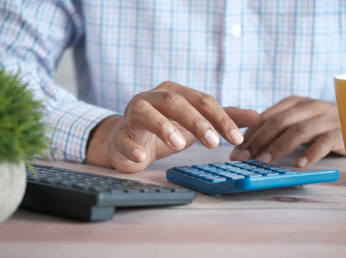 Main utilisant une calculatrice sur un bureau en bois, pour estimer une charge déductible de site internet
