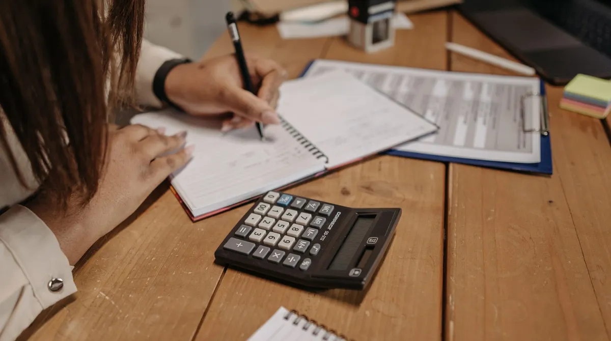 Bureau en bois avec calculatrice, notes manuscrites et documents comptables, agence web Brest