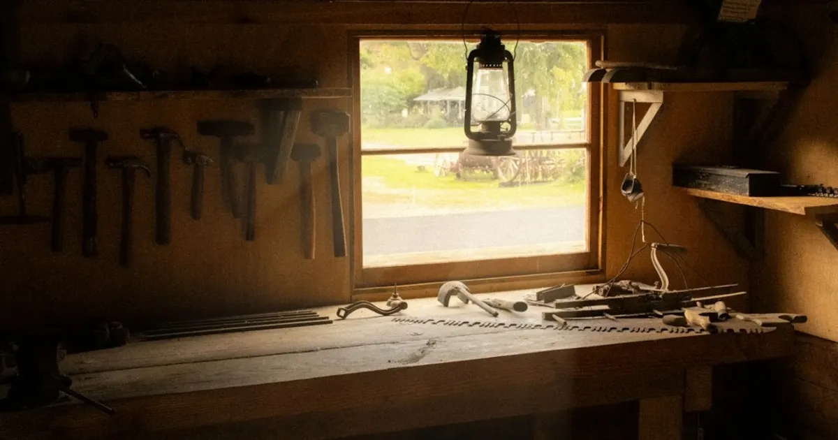Établi d'atelier en bois sous une fenêtre, outils accrochés au mur, lumière chaude