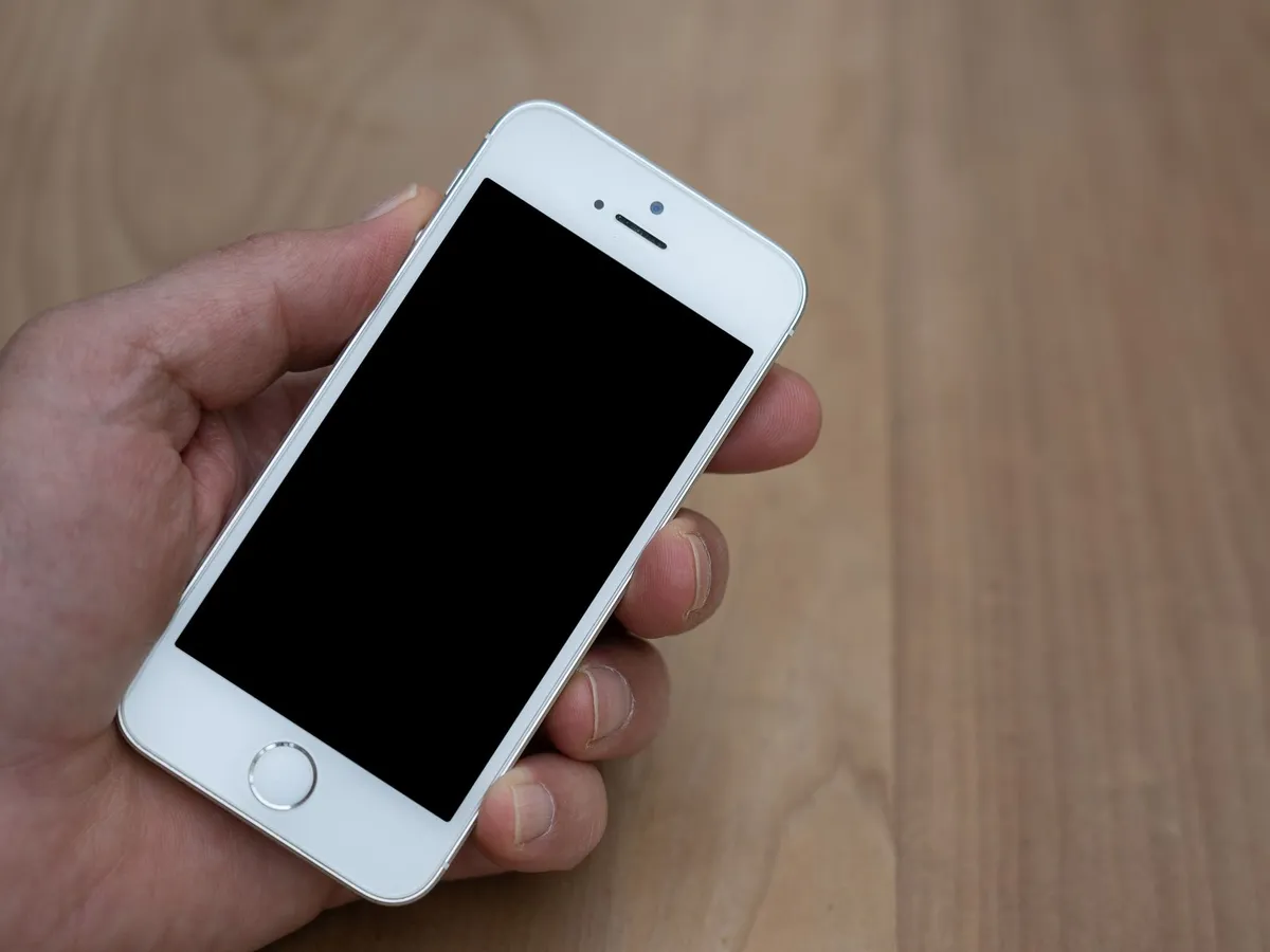 Main tenant un smartphone à l'écran noir, posé sur un établi en bois, prêt à envoyer une demande d'avis Google