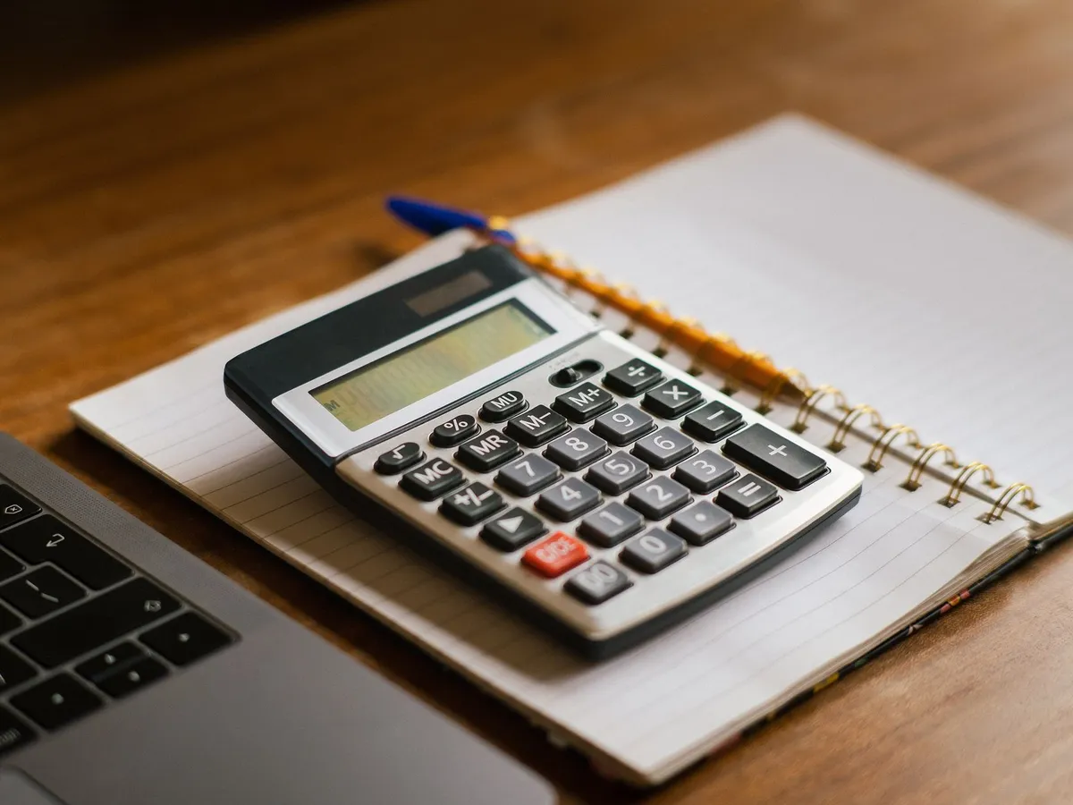 Calculatrice posée sur un carnet ouvert à côté d'un ordinateur portable, bureau en bois