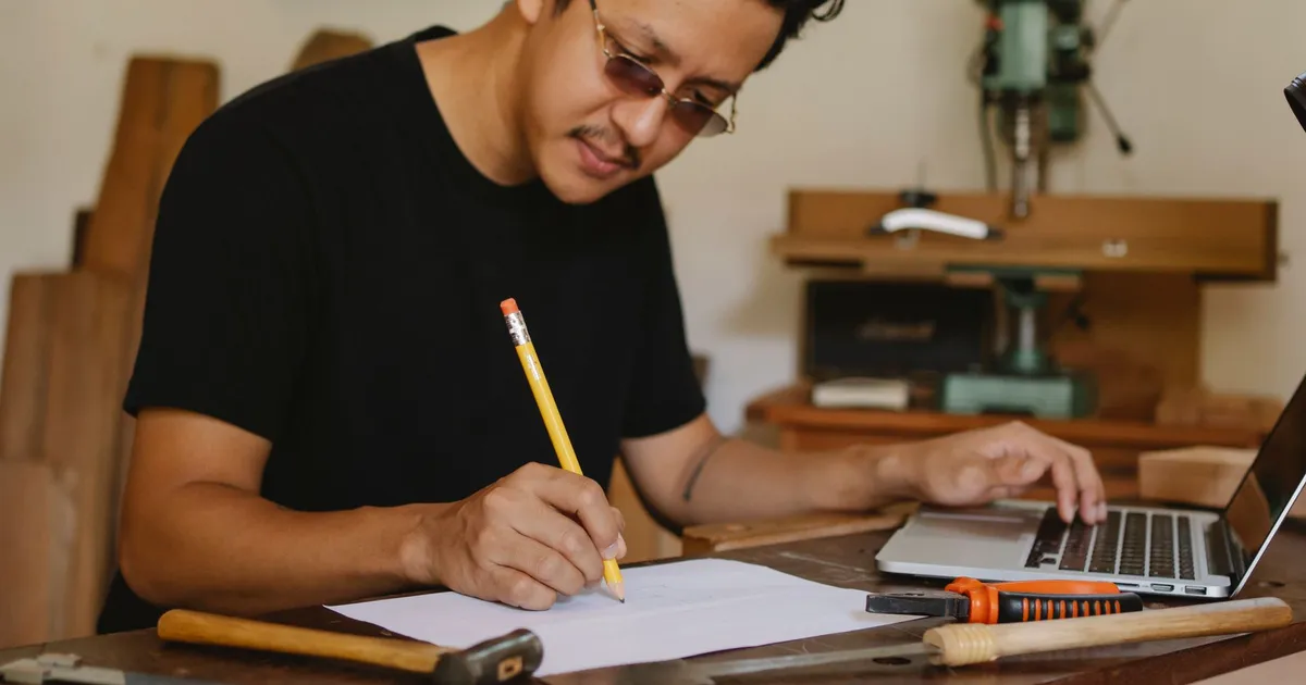 Artisan prenant des notes au crayon près de son ordinateur portable dans son atelier bois
