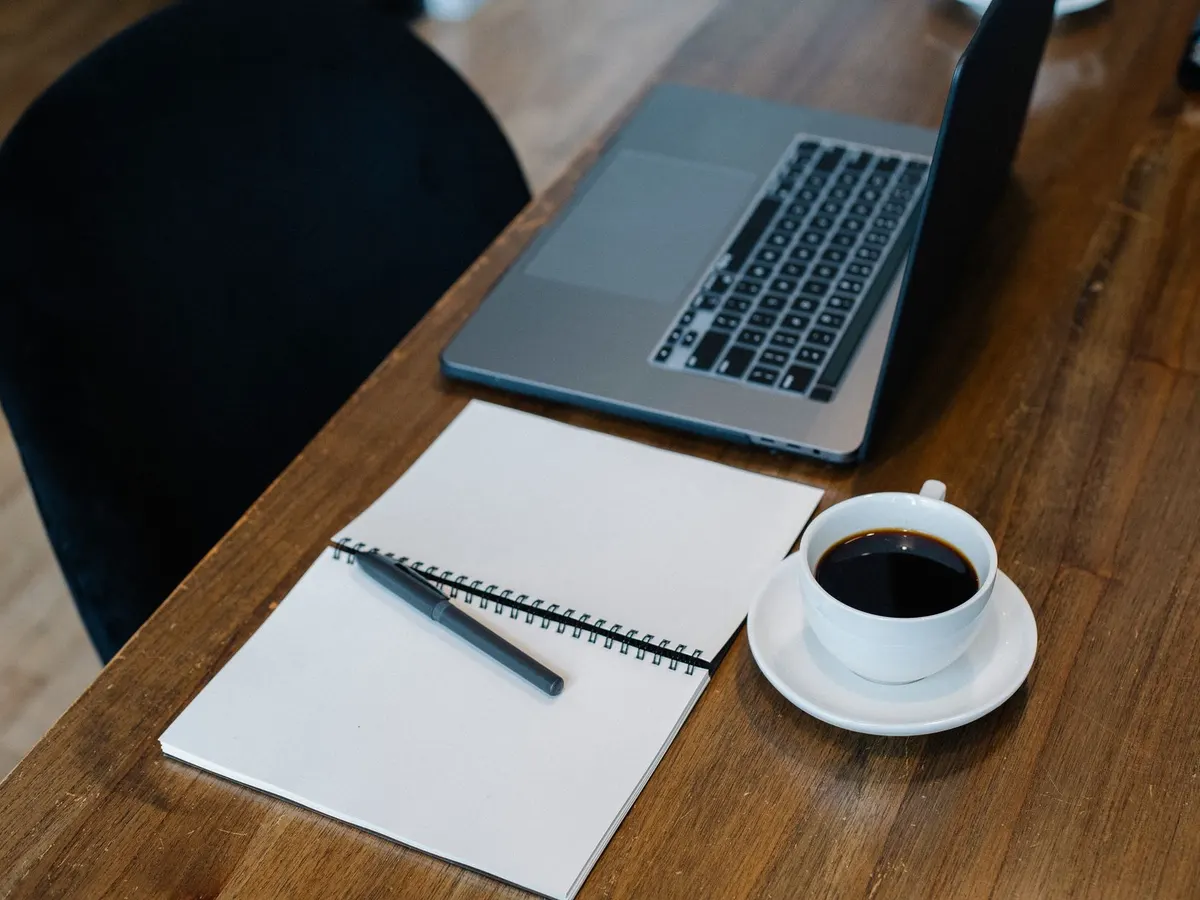 Ordinateur portable, bloc à spirale et tasse de café sur un bureau en bois, de quoi préparer l'inventaire avant la bascule