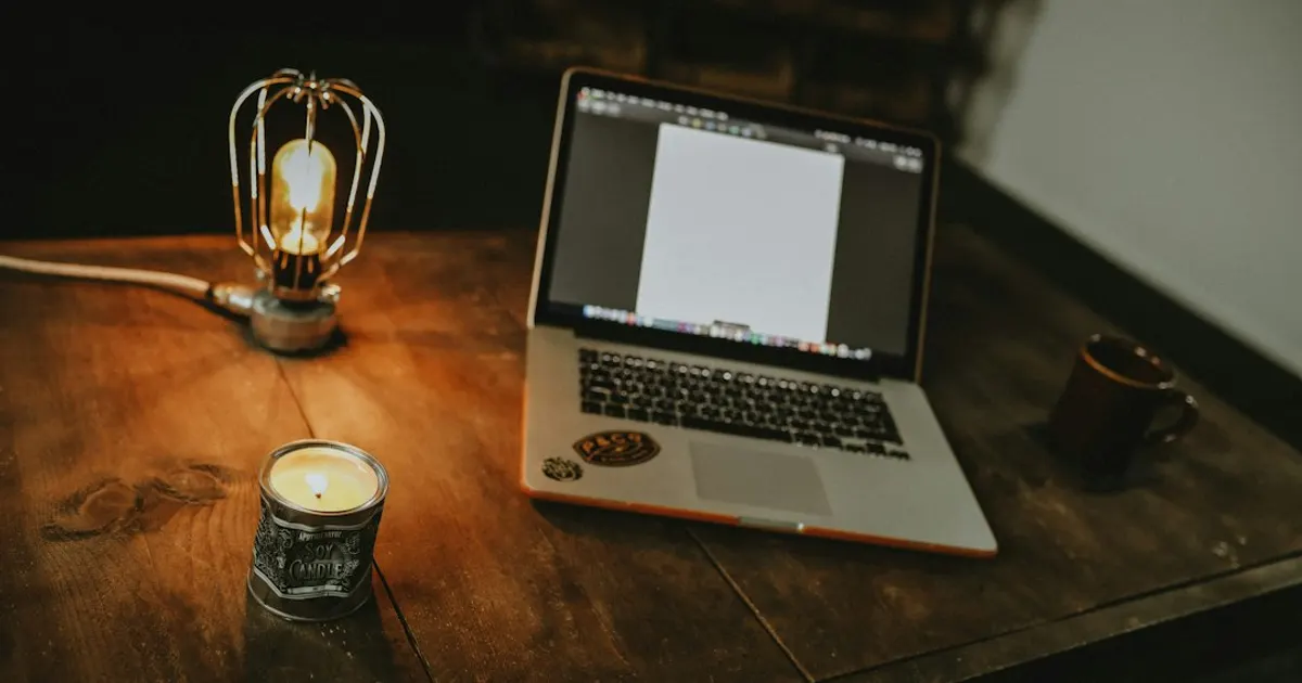 Ordinateur portable ouvert sur une table en bois sombre, éclairée par une lampe à filament, ambiance d'atelier