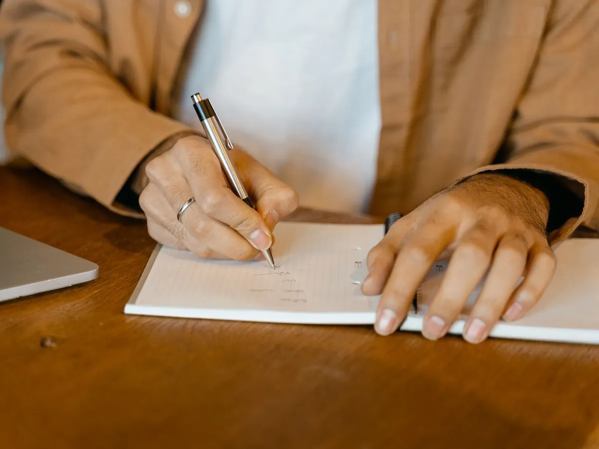 Main annotant un carnet à côté d'un ordinateur portable, relecture des clauses d'un contrat de maintenance