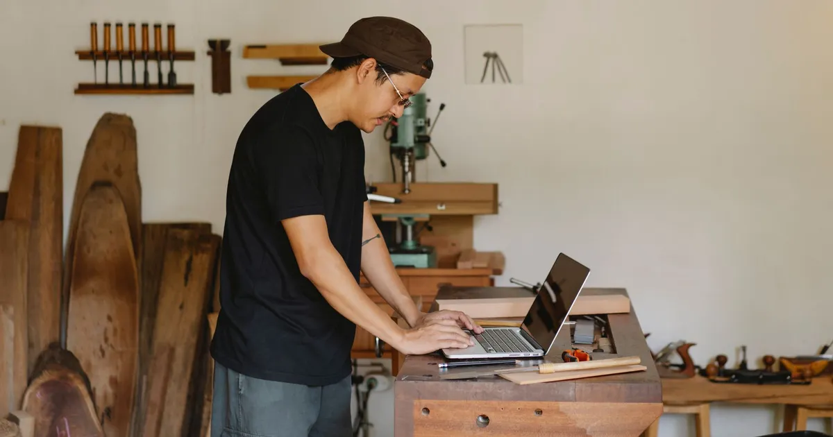 Artisan de profil sur son ordinateur portable dans son atelier bois, avant de signer un contrat de maintenance