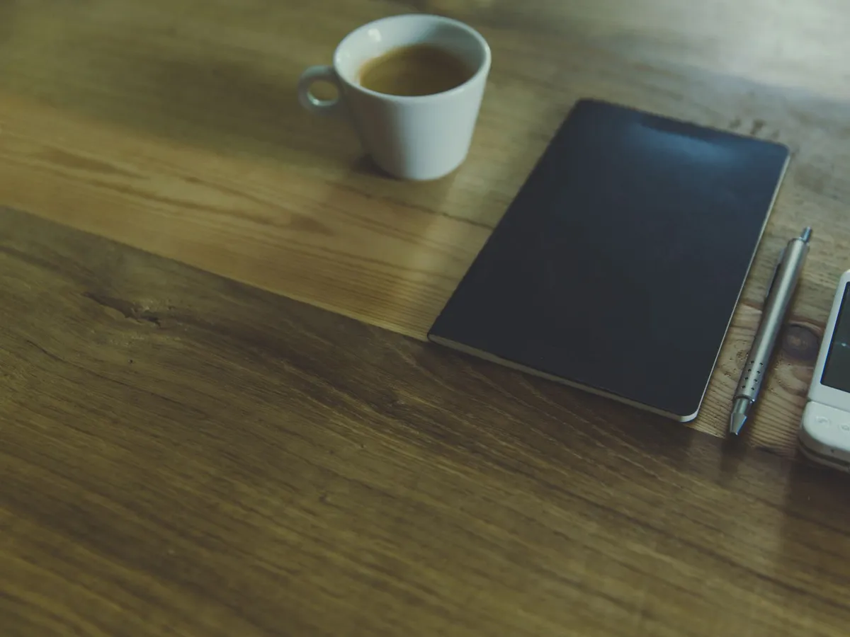 Carnet fermé, stylo et téléphone posés sur un bureau en bois, le temps de patienter avant de rappeler son prestataire