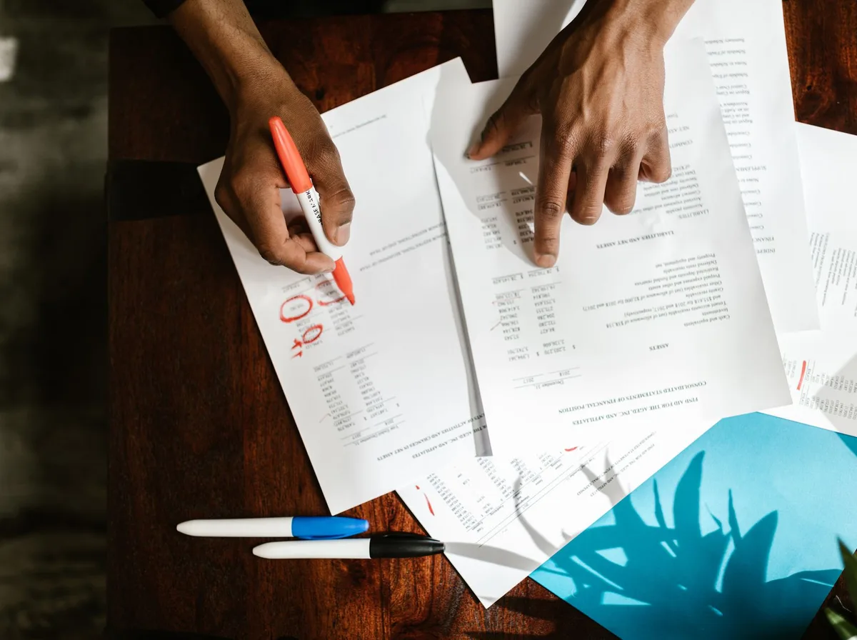 Mains annotant au marqueur rouge des documents de comparaison posés sur un bureau en bois