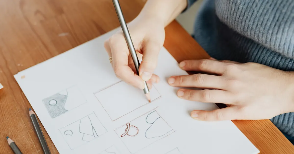 Mains dessinant des pistes de logo au crayon sur une feuille, sur un bureau en bois