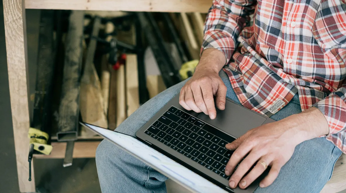 Artisan consultant un ordinateur portable sur son établi d'atelier, mains sur le clavier