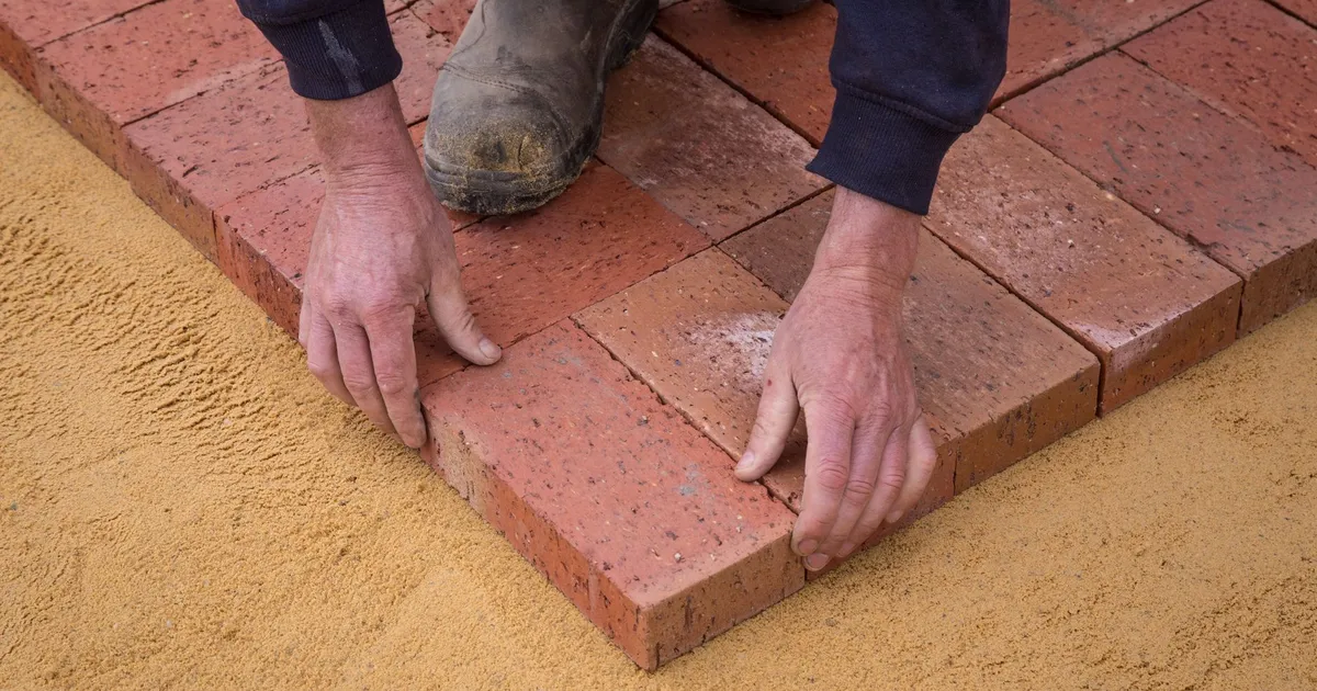 Mains d'un maçon posant des pavés de terre cuite sur un lit de sable, chantier de maçonnerie en Bretagne