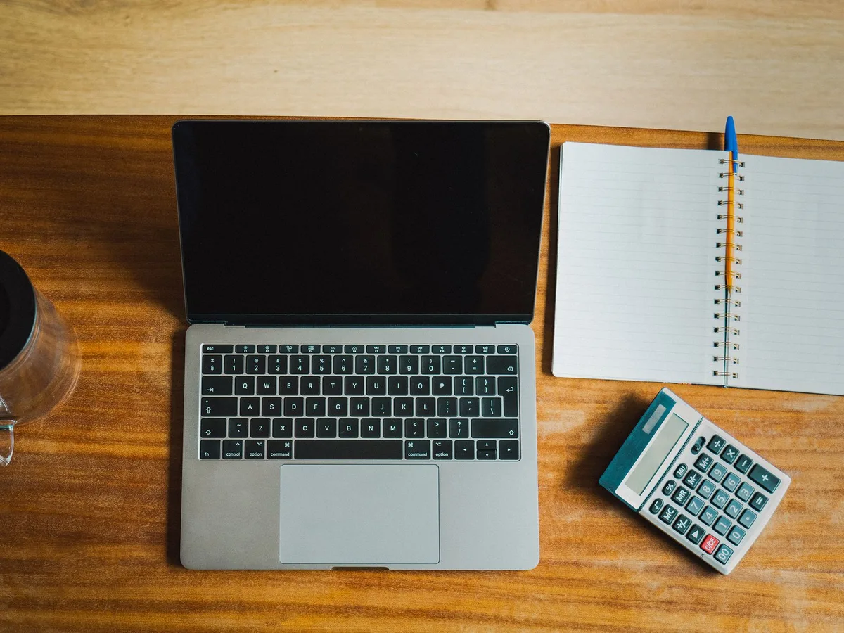 Ordinateur portable, carnet et calculatrice sur un bureau en bois, pour vérifier un budget avant de payer un site internet