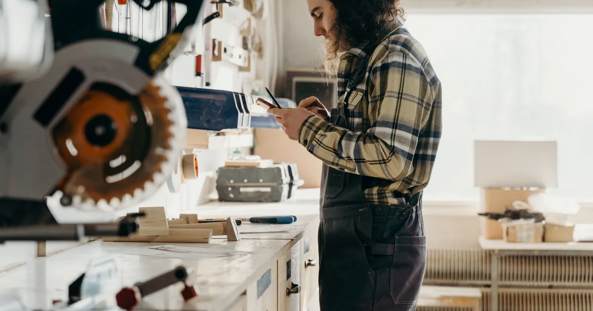 Artisan menuisier consultant son téléphone dans son atelier bois avant de se décider