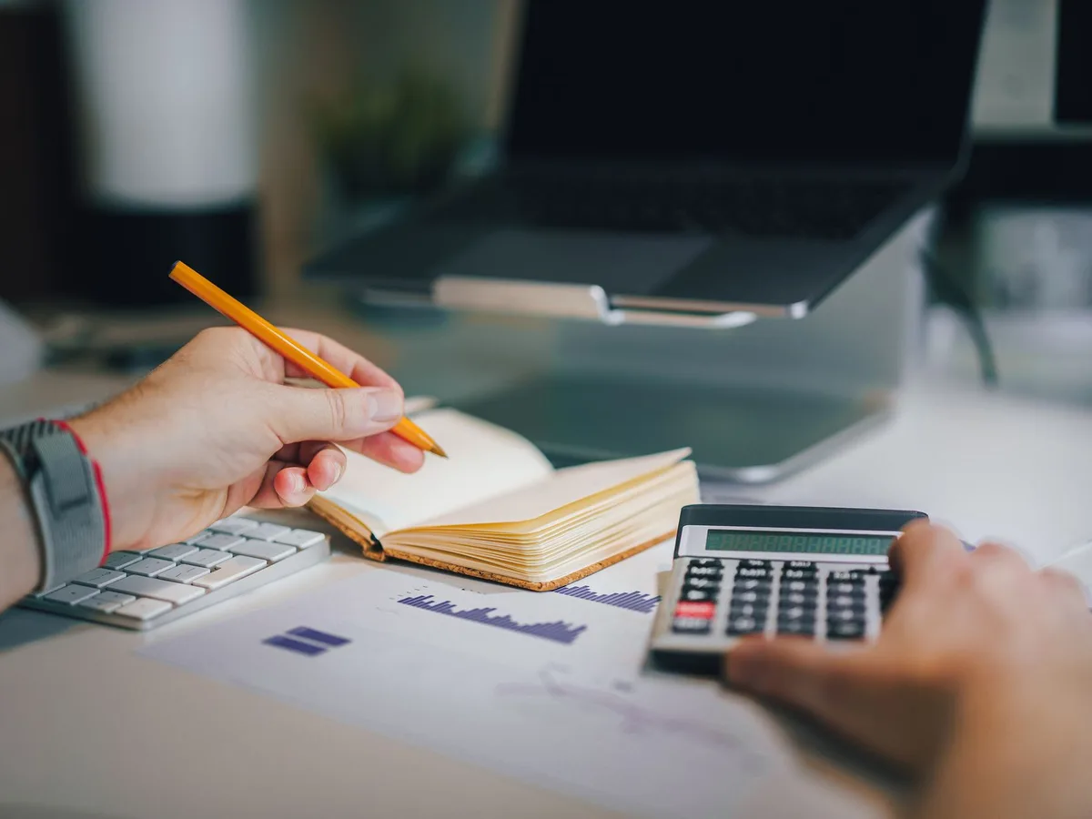 Main faisant un calcul à la calculatrice à côté d'un carnet de notes, pour décomposer le coût d'un abonnement site internet