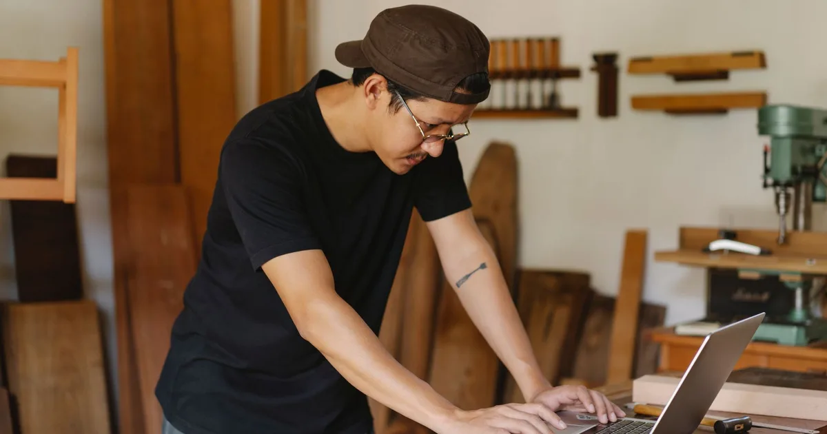 Artisan menuisier consultant son ordinateur portable sur l'établi de son atelier