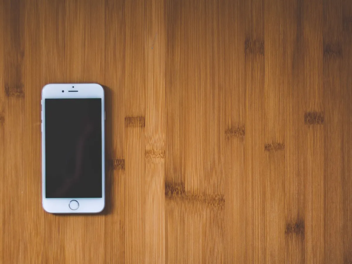 Smartphone posé sur un plan de travail en bois, de quoi envoyer sa demande de témoignage par SMS