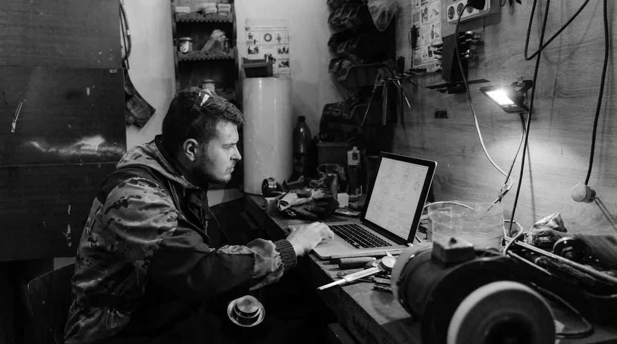Artisan de profil devant son ordinateur portable dans son atelier, outils au mur : demander un témoignage client