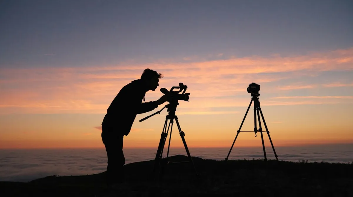 Silhouette d'un vidéaste réglant sa caméra sur trépied face à un lever de soleil, TikTok artisan